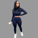 Woman in navy blue athletic outfit standing against a gray wall.