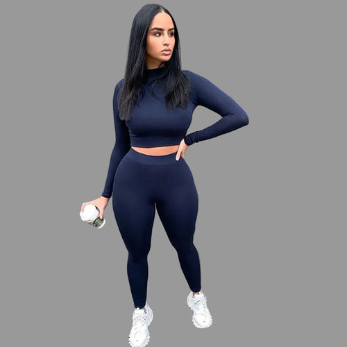 Woman in navy blue athletic outfit standing against a gray wall.