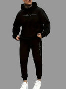 Man wearing a black hoodie and pants with a logo on a street.