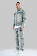 Person wearing a distressed denim jacket and jeans on a gray background
