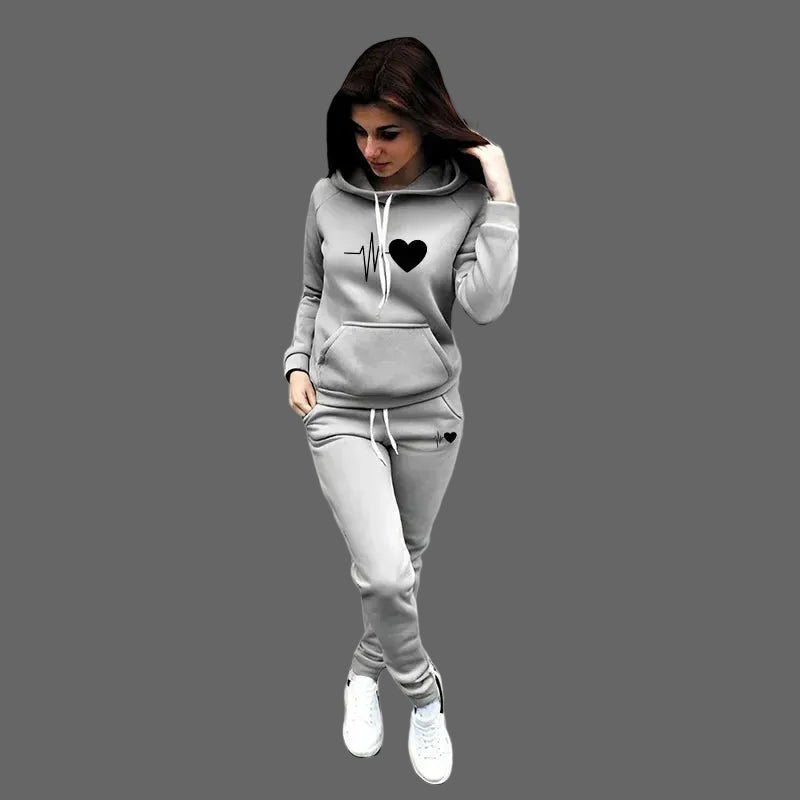 Woman wearing a gray hoodie and pants set with a heart design on a plain background