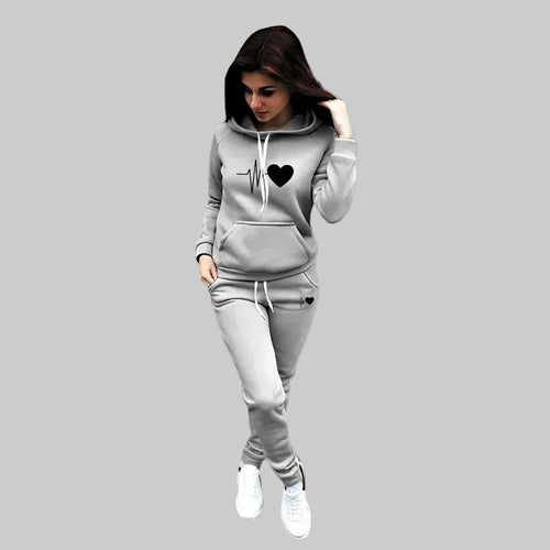 Woman wearing a gray hoodie and pants set with a heart design on a plain background