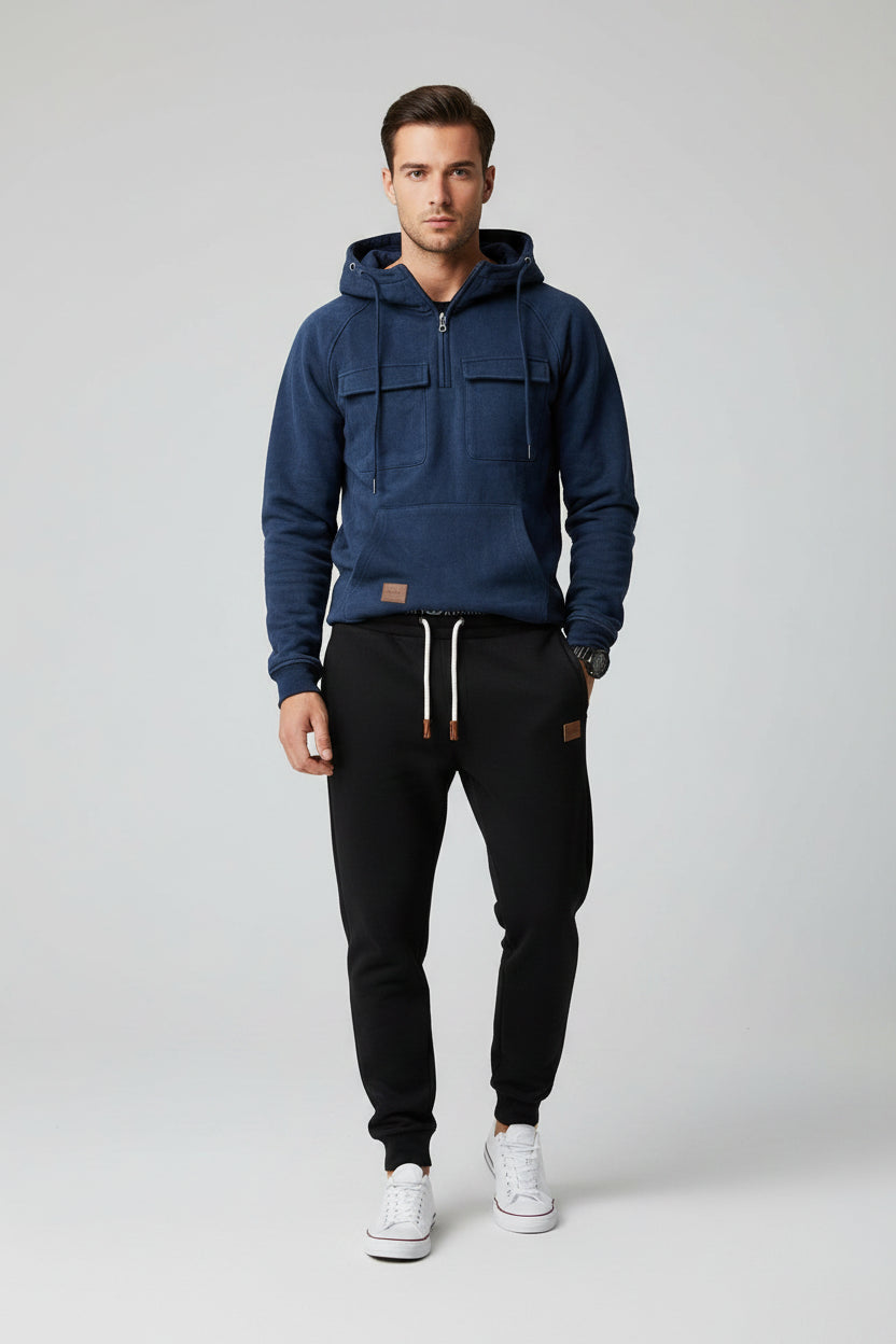 Blue hoodie with front pockets and a person wearing black pants and white sneakers on a gray background