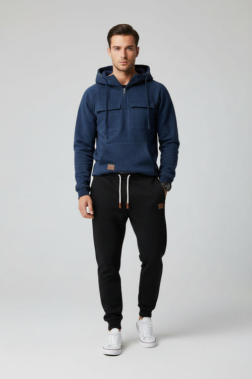 Blue hoodie with front pockets and a person wearing black pants and white sneakers on a gray background
