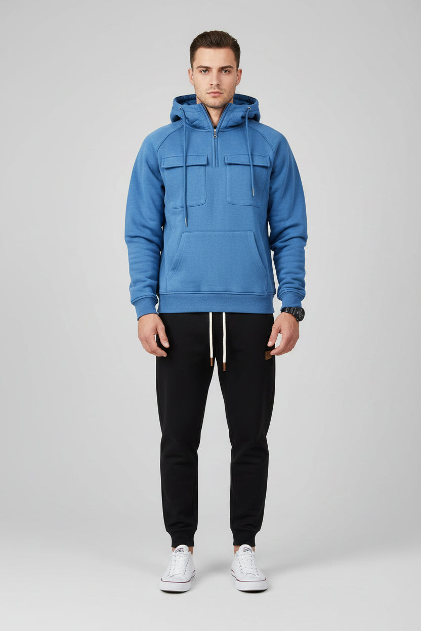 Blue hoodie with front pockets and a person wearing black pants and white sneakers on a gray background