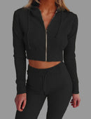 Person wearing a black ribbed zip-up hoodie and matching pants on a plain background
