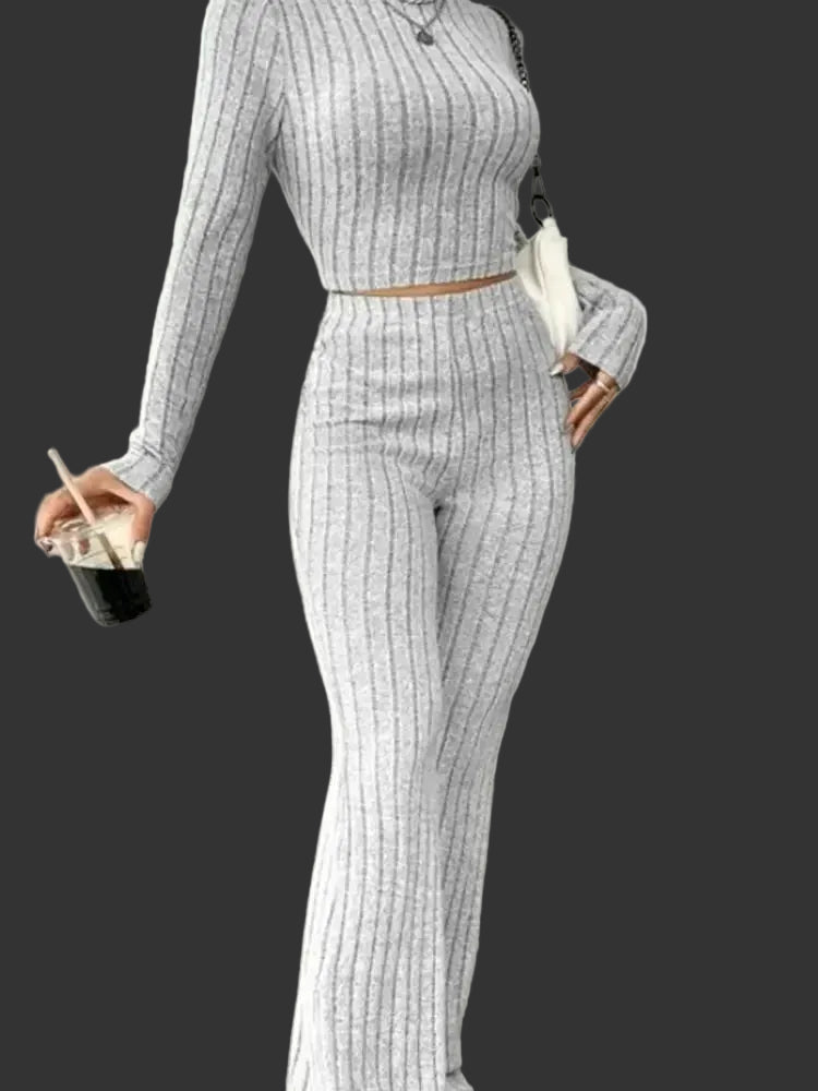 Person wearing a gray ribbed outfit holding a drink in a minimal indoor setting.