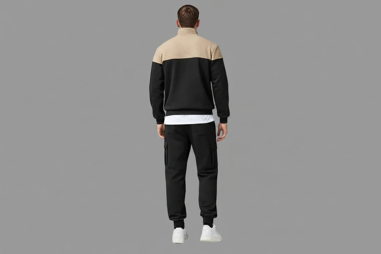 Person wearing a black and beige tracksuit standing with a gray background