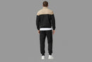 Person wearing a black and beige tracksuit standing with a gray background