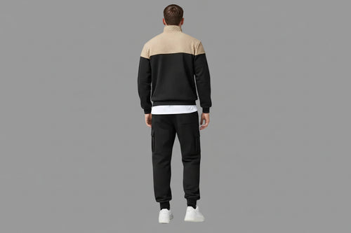 Person wearing a black and beige tracksuit standing with a gray background
