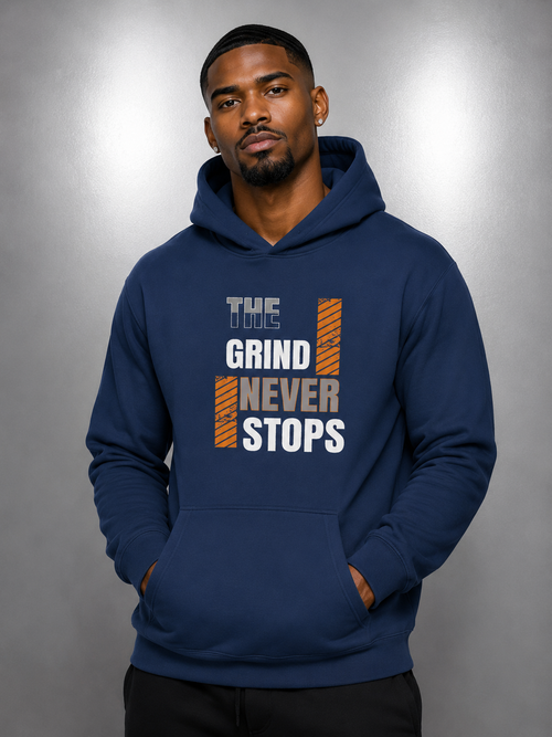 A man wearing a navy blue pullover hoodie with a graphic print on the chest that reads 'THE TOYS GRIND NEVER STOPS' in white and orange, posed against a gray studio background.