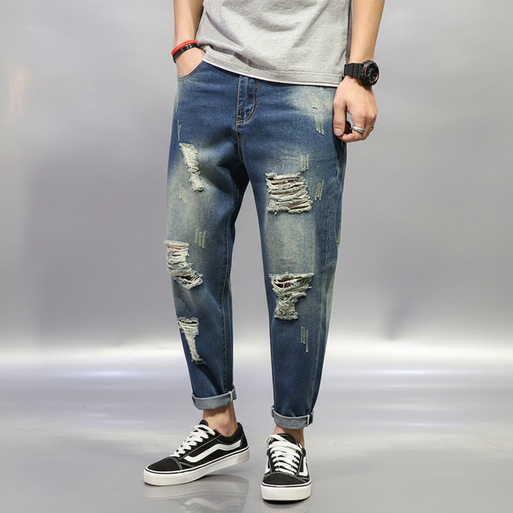 Person wearing ripped blue jeans and black and white sneakers on a dark background