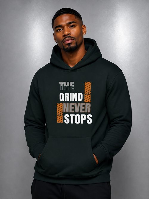 A man wearing a dark forest green hoodie with a graphic print that reads 'THE GRIND NEVER STOPS' in white and orange, posed against a gray studio background.